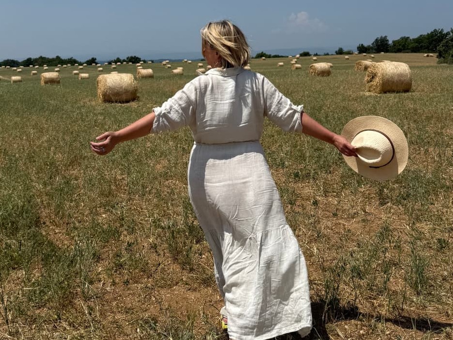 D LeD walking through a sunlit hay field holding a straw hat